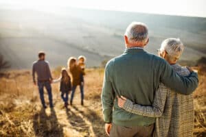 Back view of embraced grandparents enjoying while looking at their family on a field in autumn day. Happy they have completed their estate planning and used a CPA to help.
