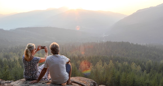 Mature couple relax on mountain ledge, look out to view with no worries of tax changes after retirement because they have hired a CPA.