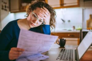 Young brunette curly female reading her bill papers, looking stressed over tax problems.