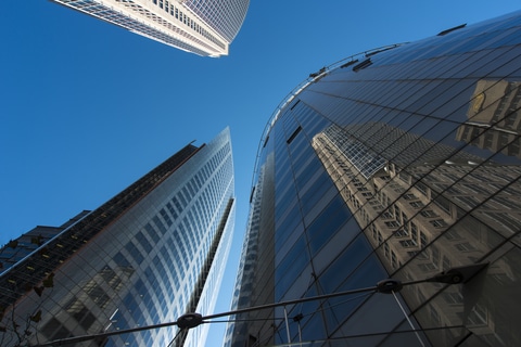 Looking up at blue sky through corporate skyscrapers with reflections of other buildings to note the Corporate Transparency Act.