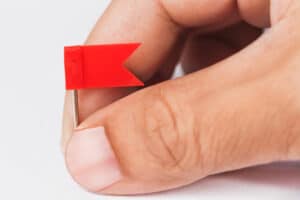 Isolated male hand with plastic red flags pin demonstrating red flags that can trigger a tax audit. Brown Chism & Thompson can help.