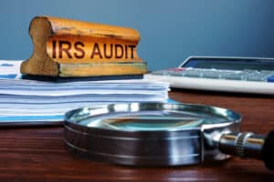 Stamp IRS audit and accounting documents with magnifying glass. Why Does the IRS Audit People Top Reasons Explained - Brown, Chism & Thompson