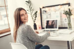 Young female freelancer at home office winter writing in planner turned looking back smiling. self-employed taxes - freelance CPA - Brown, Chism & Thompson