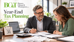 Accountant and small business woman sitting at desk with laptop, documents and receipts, discussing year-end tax planning.